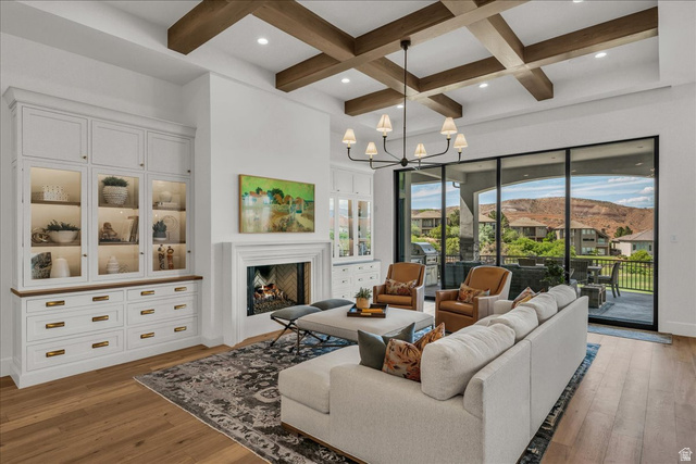 2608 Canyon Ridge Drive St. George, UT 84770 - Photo 10 of 86 Living area featuring wood-finish flooring, a coffered ceiling with exposed wood beams, a fireplace with a white mantel, and built-in white cabinetry with glass display doors