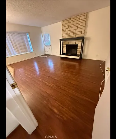 a view of an empty room with wooden floor fireplace and a window