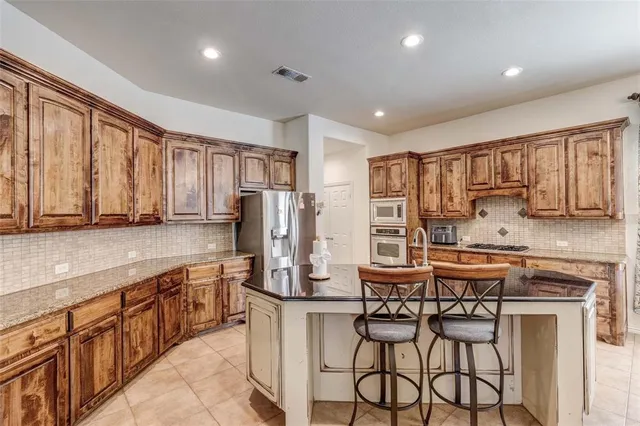 a kitchen with stainless steel appliances kitchen island granite countertop a refrigerator a stove top oven and a sink with wooden floor