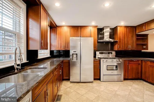 a kitchen with stainless steel appliances granite countertop a refrigerator a stove and a sink with wooden cabinets