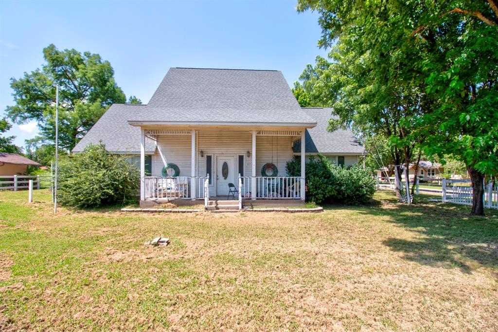 503 Sherman Street Tioga, TX 76271 - Photo 1 of 13 White siding residence featuring a covered front porch with white railing, a gray shingle roof, and mature trees providing natural shade