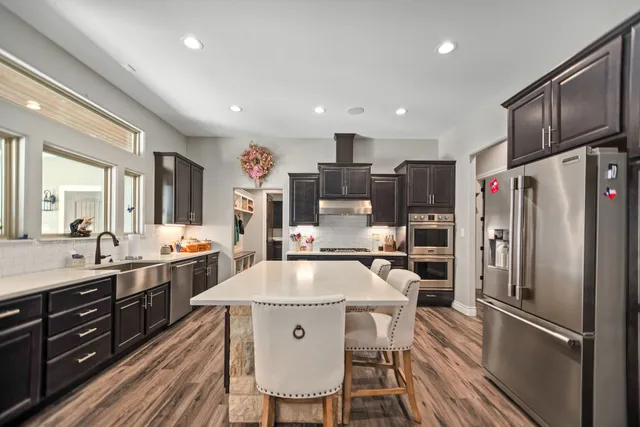 a kitchen with stainless steel appliances granite countertop a refrigerator a sink dishwasher a stove and white cabinets with wooden floor