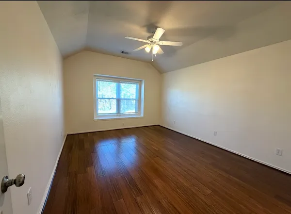an empty room with wooden floor fan and windows
