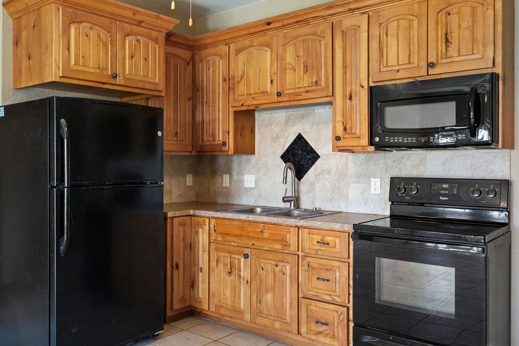 1101 Crider Road Marble Falls, TX 78654 - Photo 33 of 34 Kitchen featuring black appliances, decorative backsplash, light countertops, light tile patterned floors, and brown cabinetry