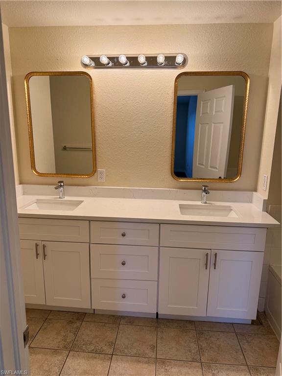 7985 Preserve Circle, Unit 1133 Naples, FL 34119 - Photo 19 of 36 Full bath with double vanity, light tile patterned floors, and a textured wall