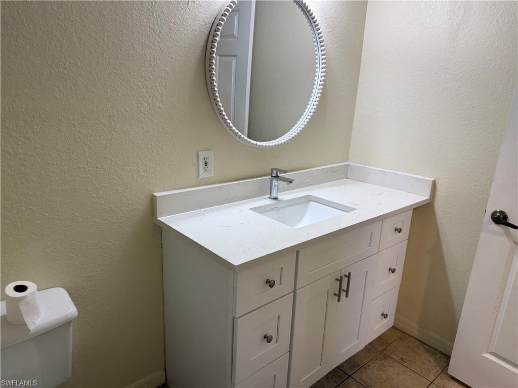 7985 Preserve Circle, Unit 1133 Naples, FL 34119 - Photo 26 of 36 Half bath featuring a textured wall, vanity, and light tile patterned flooring