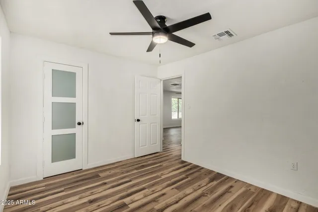 a view of an empty room with wooden floor and a ceiling fan