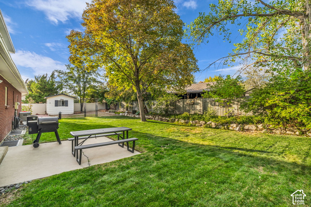 1073 Pineridge Road Sandy, UT 84094 - Photo 27 of 31 Expansive grass lawn, mature trees, concrete patio, brick exterior, and a detached shed