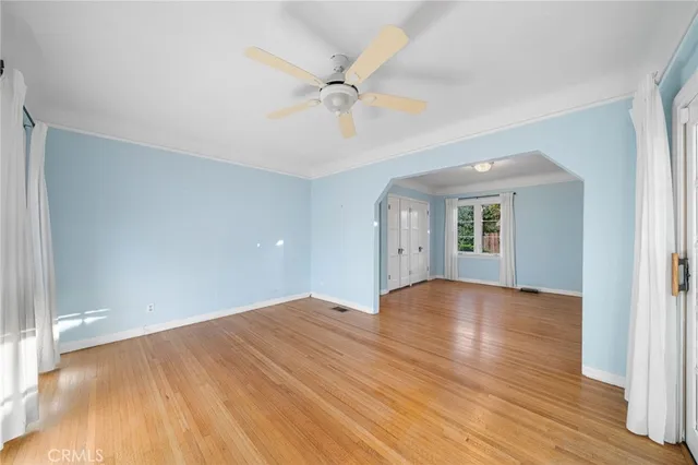 a view of an empty room with wooden floor and a ceiling fan