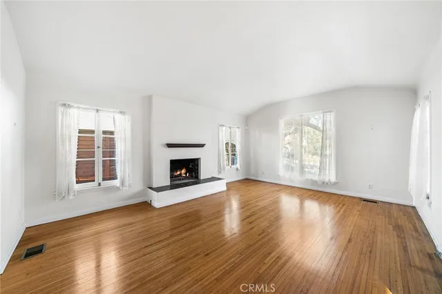 an empty room with wooden floor fireplace and windows