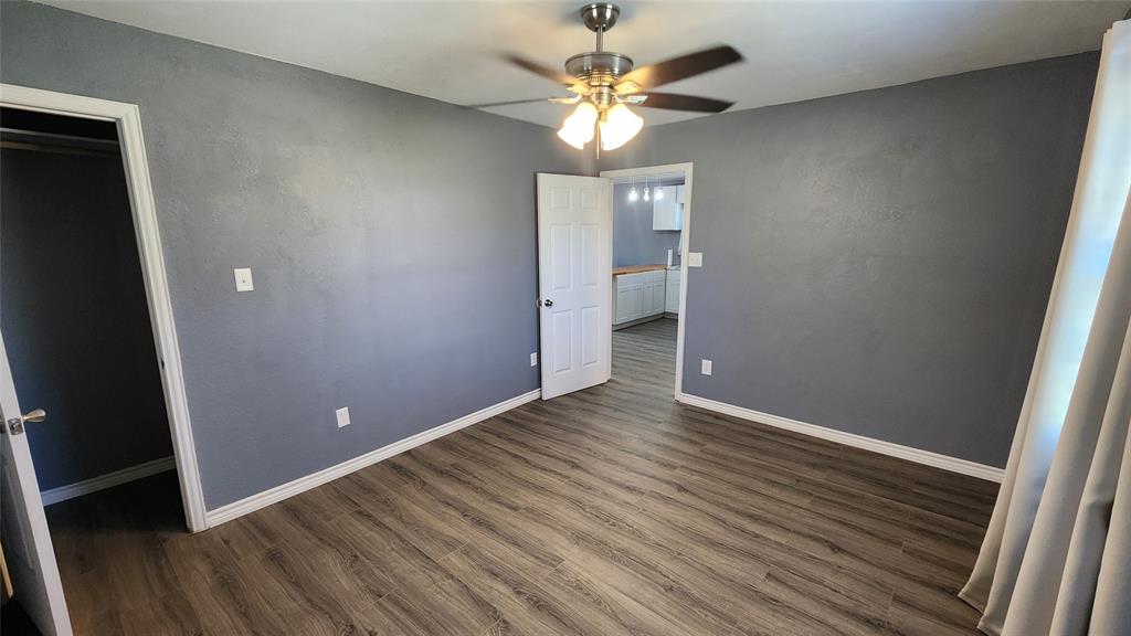 809 Bowie Street Sweetwater, TX 79556 - Photo 13 of 20 Unfurnished bedroom with dark wood-style floors, baseboards, and a ceiling fan