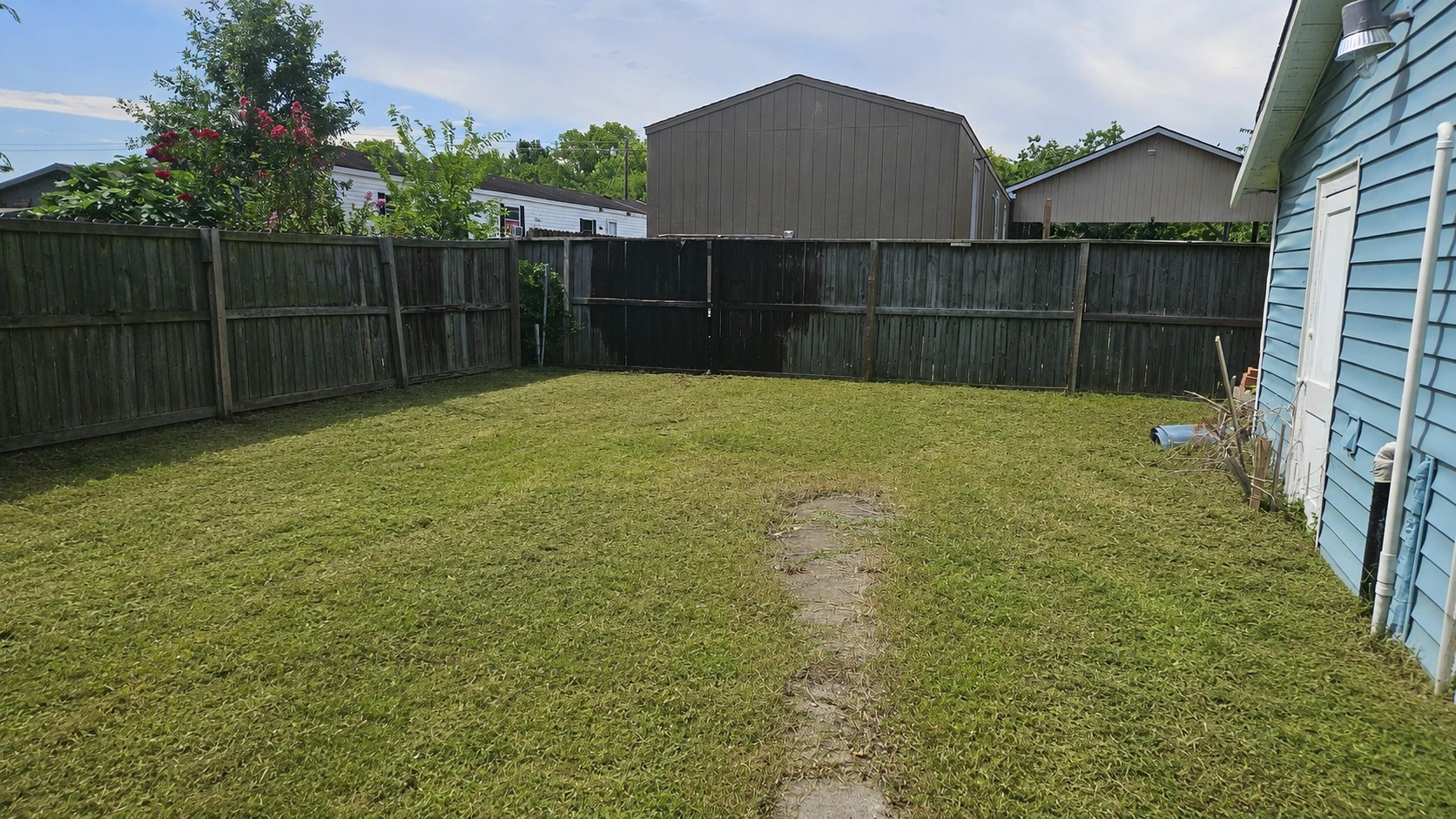 2415 Perry Street Baytown, TX 77521 - Photo 19 of 23 Fenced backyard with well-maintained grass, a small path, and a blue-sided house on the right. Ideal for outdoor activities or gardening.