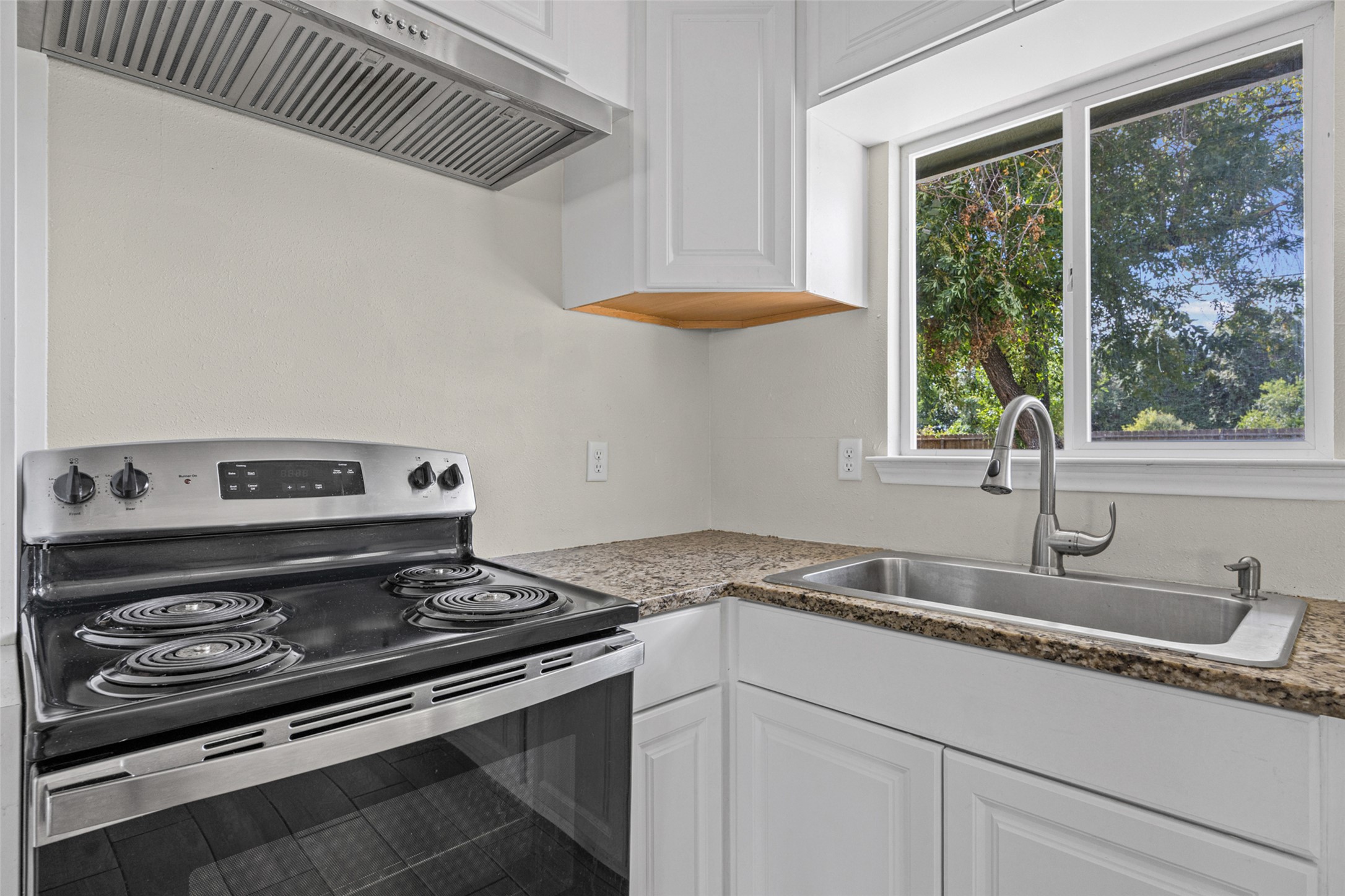 Natural light pours through the window over the durable granite countertops and modern cooktop area.