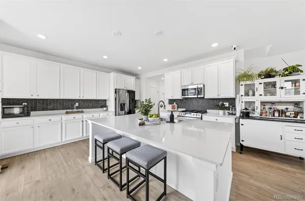 a kitchen with stainless steel appliances granite countertop a stove top oven a sink a refrigerator white cabinets and couches with wooden floor