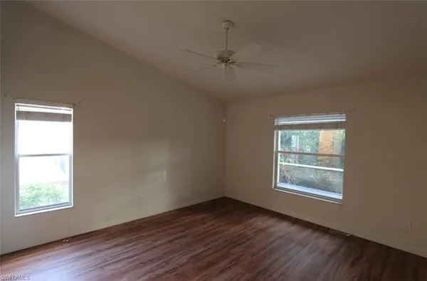 an empty room with wooden floor windows and fan