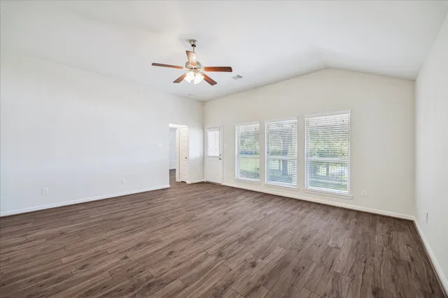 an empty room with wooden floor fan and windows