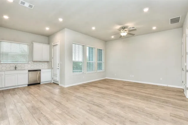 a view of an empty room with kitchen and window
