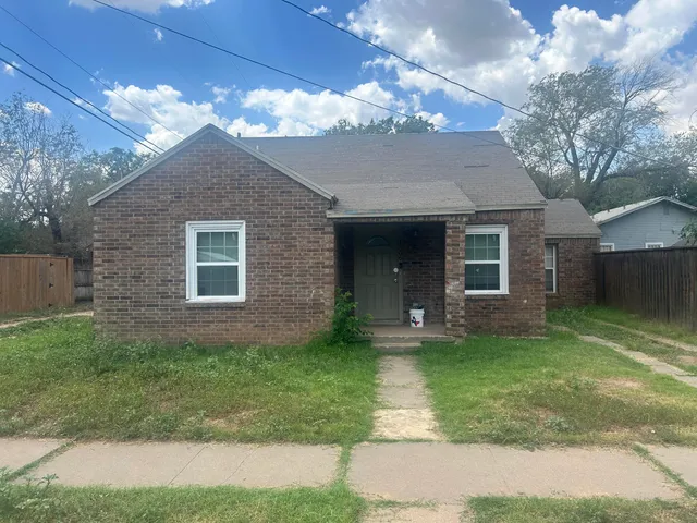 a view of a brick house next to a yard with a large tree