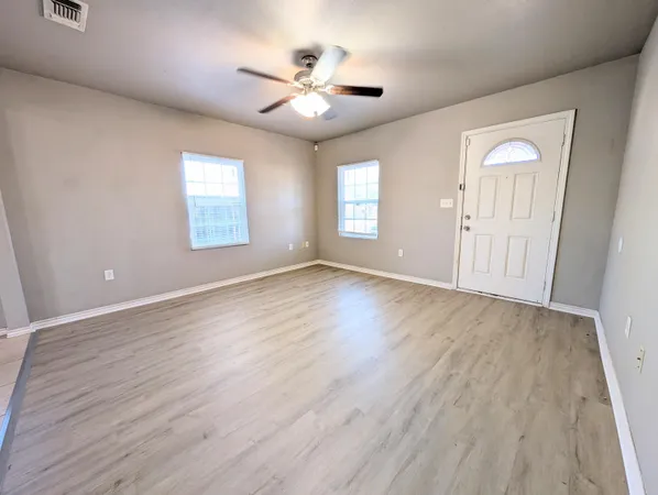 an empty room with wooden floor chandelier fan and windows