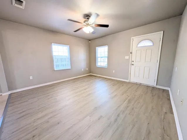 an empty room with wooden floor chandelier fan and windows