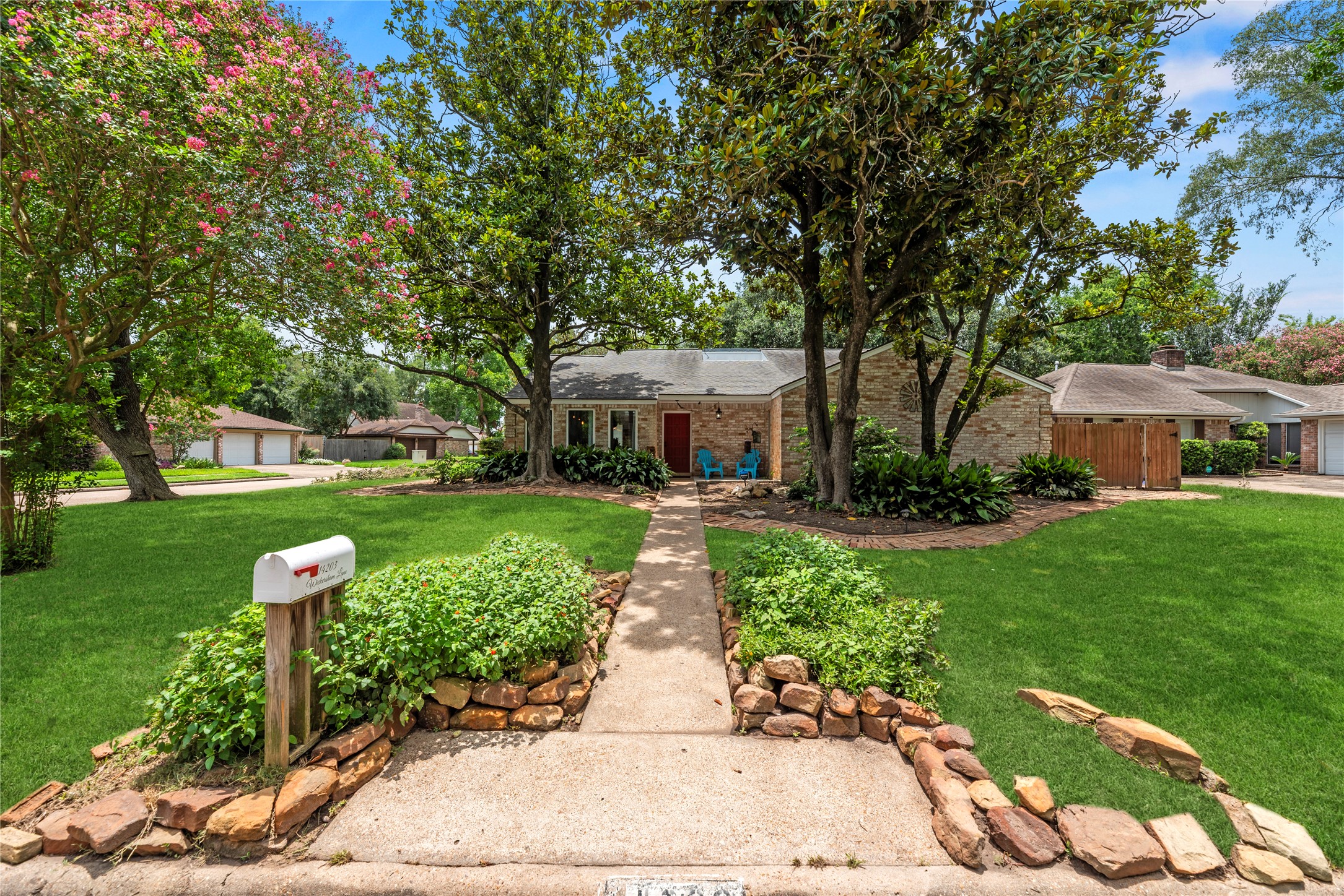 14203 Wickersham Lane Houston, TX 77077 - Photo 25 of 25 Front exterior perspective capturing the home’s exceptional curb appeal from the street, featuring a classic brick facade, established landscaping, natural stone-edged garden beds, and towering trees.