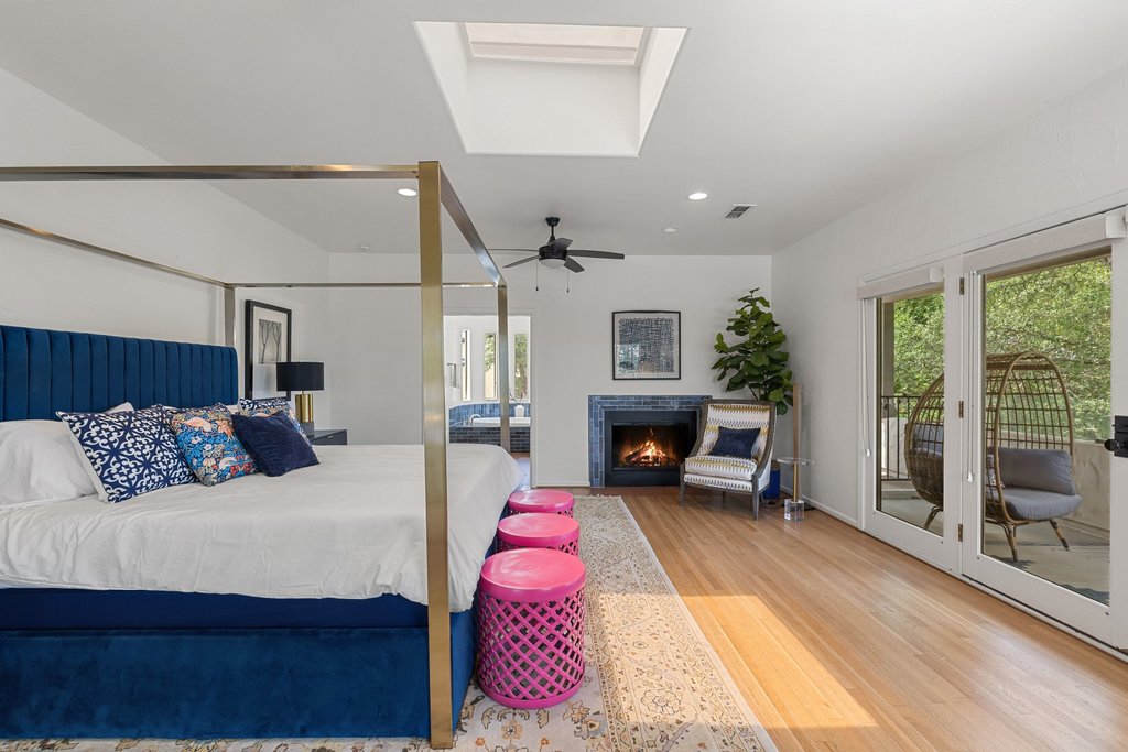 716 North Commons Ford Road Austin, TX 78733 - Photo 10 of 30 Bright interior space featuring a skylight, wood-finish flooring, a fireplace with a tiled surround, a ceiling fan, and glass paneled doors opening to an exterior balcony