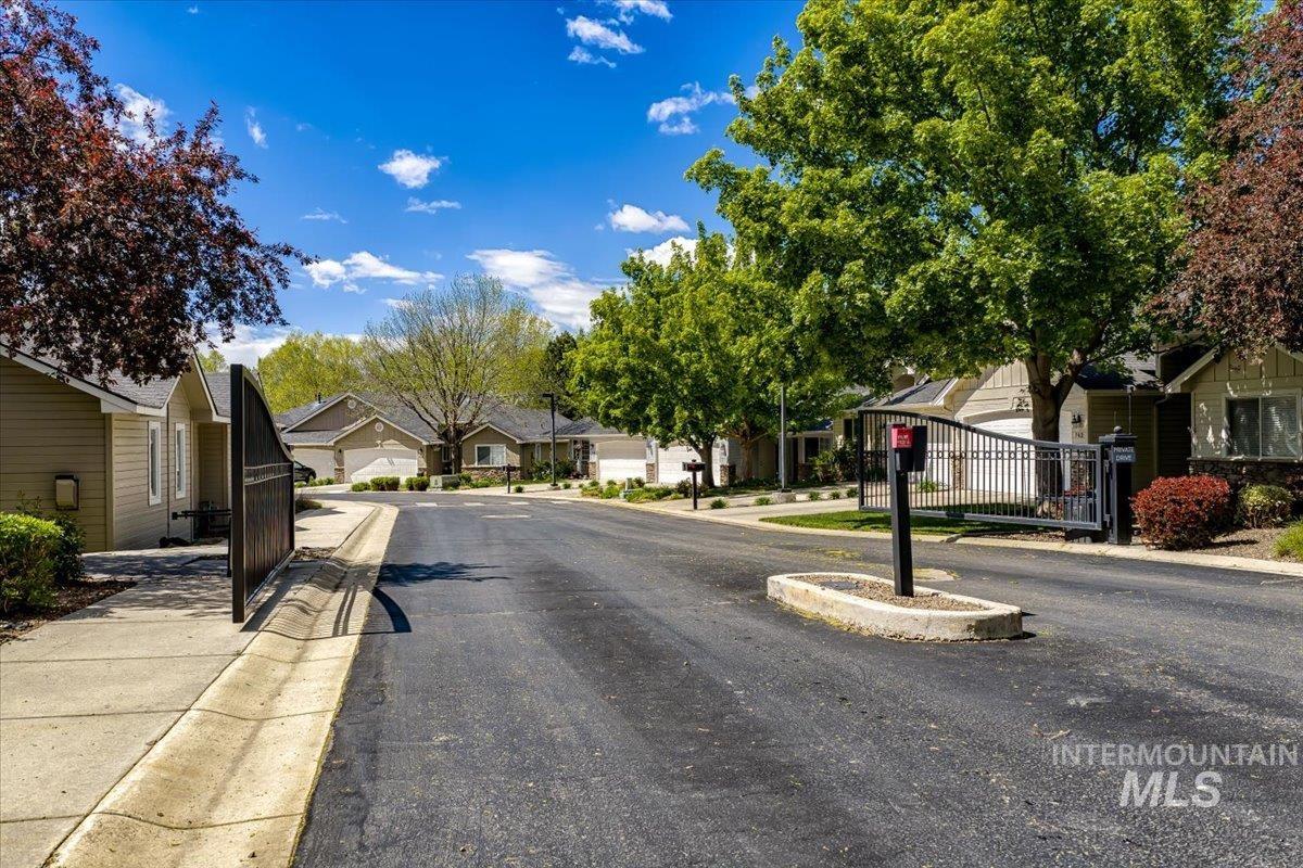 725 North Eagle Road Eagle, ID 83616 - Photo 40 of 45 Gated community entrance featuring wrought iron gate, paved roadway, mature landscaping, and single-story residences with attached garages