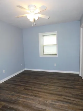 a view of an empty room with wooden floor and a fan