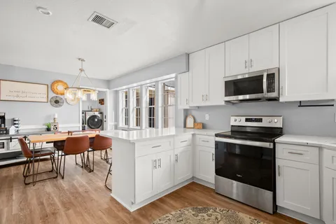 a kitchen with stainless steel appliances kitchen island granite countertop a stove a sink dishwasher and white cabinets with wooden floor