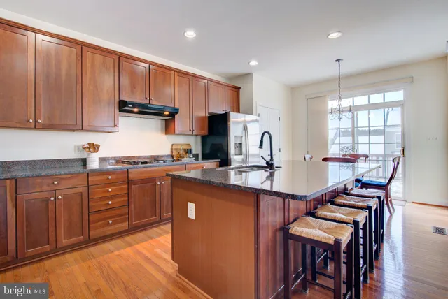 a kitchen with stainless steel appliances granite countertop a stove top oven a sink dishwasher and a refrigerator with wooden cabinets