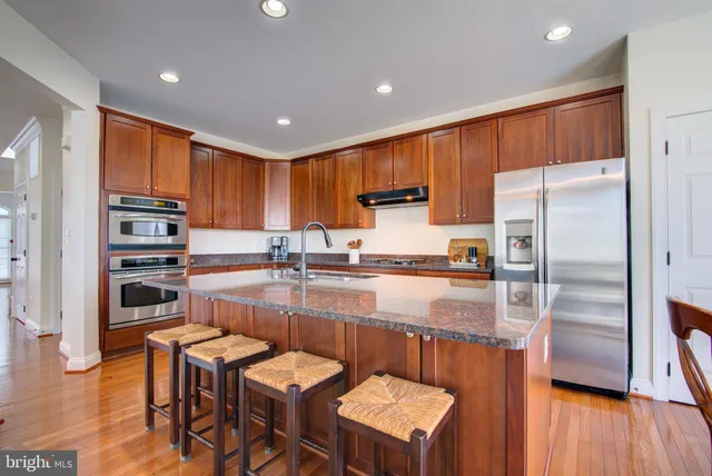 a kitchen with stainless steel appliances granite countertop a refrigerator a sink a stove a dining table and chairs with wooden floor