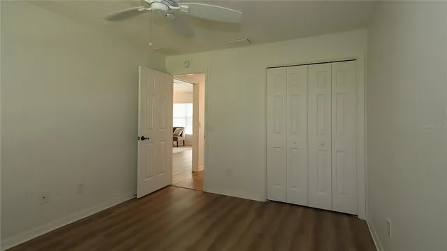 an empty room with a chandelier fan and wooden floor