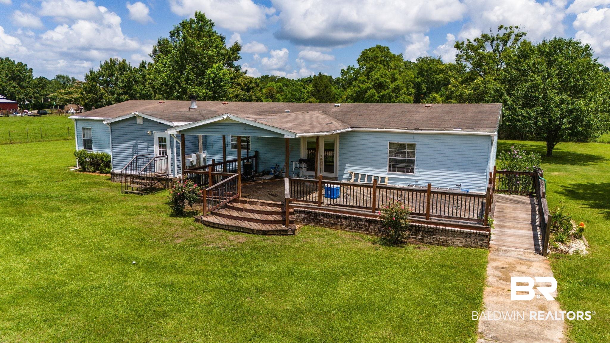 34985b Spring Road South, Unit B Stapleton, AL 36578 - Photo 2 of 31 Light blue siding residence featuring a spacious wooden deck with railings, an uncovered patio area, and a covered porch