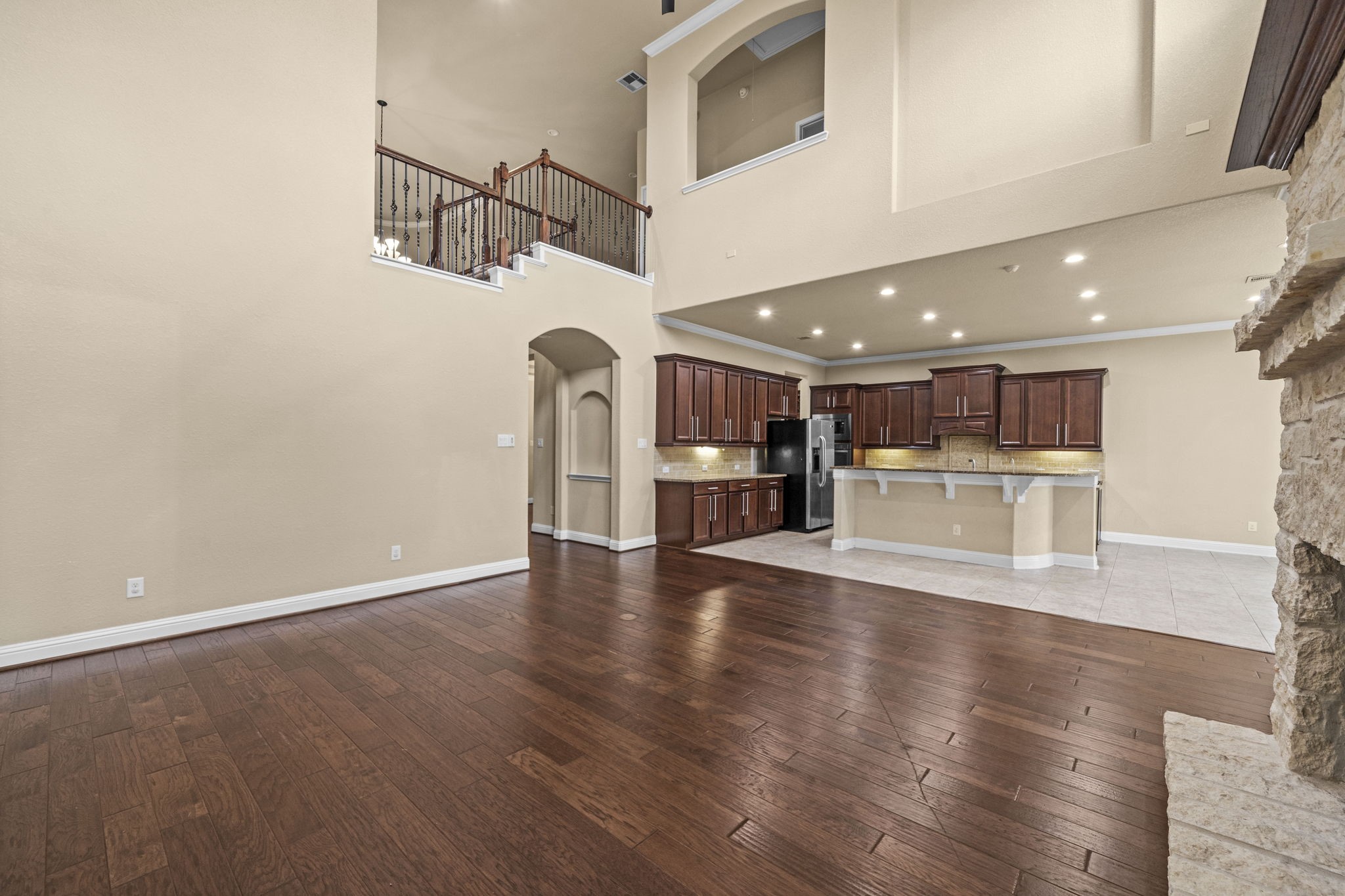 14215 Spindle Arbor Road Cypress, TX 77429 - Photo 13 of 47 This spacious open-concept living area features rich hardwood floors, high ceilings, and a view of the kitchen with dark wood cabinetry and modern appliances. A stone fireplace adds warmth to the room, while the upper balcony provides architectural interest.