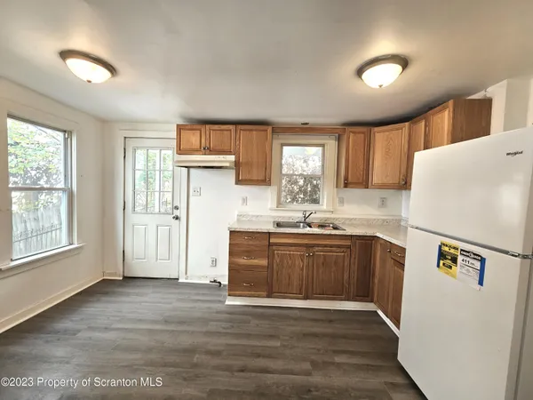 a kitchen with granite countertop a refrigerator a sink dishwasher a stove and white countertops with wooden floor