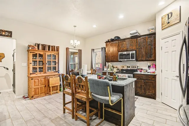 a kitchen with stainless steel appliances kitchen island granite countertop a stove a refrigerator a oven a dining table and chairs with wooden floor