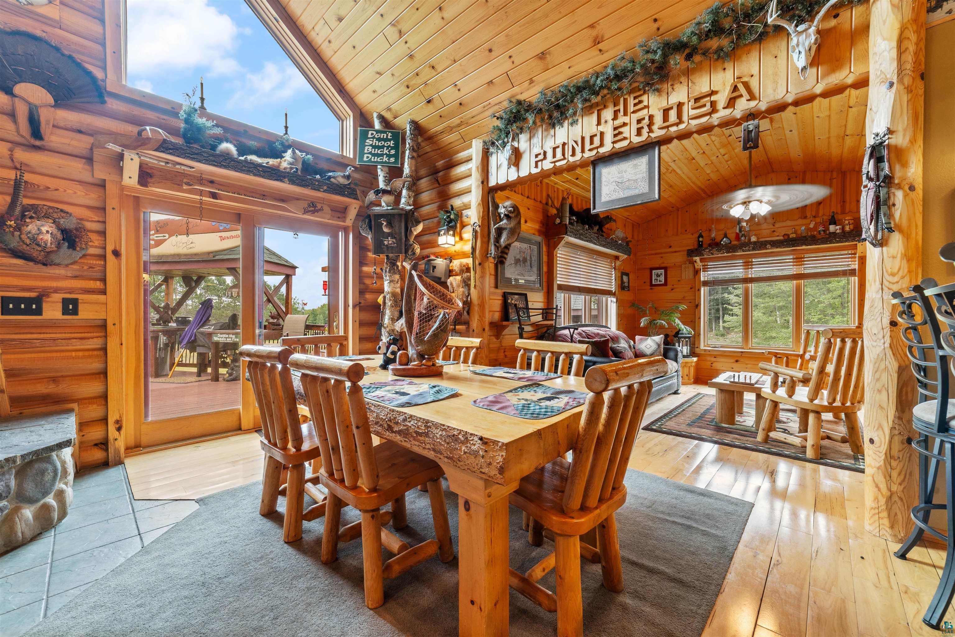11911 East Rowe Road Lake Nebagamon, WI 54849 - Photo 15 of 61 Dining area featuring natural wood walls and ceiling, a rustic wood table with matching chairs, and a large sliding glass door leading to an outdoor space