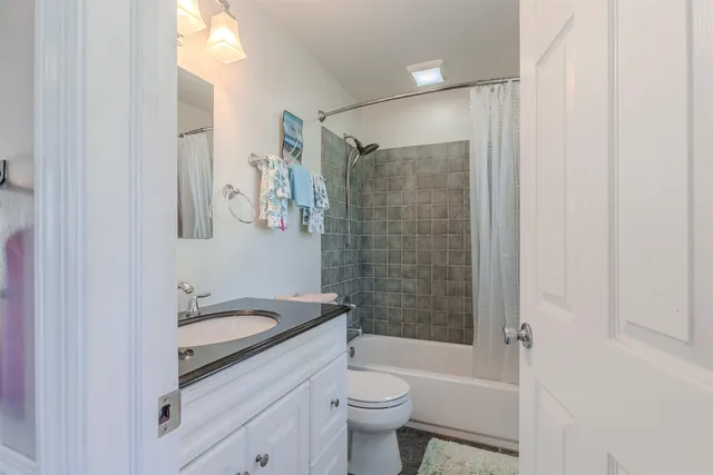 a bathroom with a granite countertop bathtub shower sink vanity and toilet