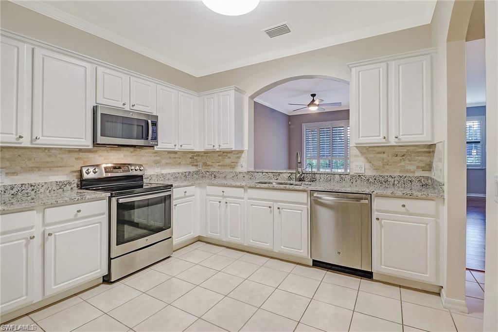 9801 Foxhall Way, Unit 4 Estero, FL 33928 - Photo 3 of 23 Kitchen featuring appliances with stainless steel finishes, backsplash, light stone countertops, white cabinetry, and crown molding