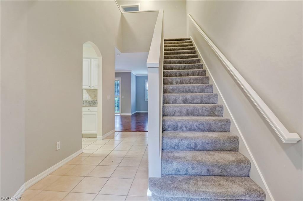 9801 Foxhall Way, Unit 4 Estero, FL 33928 - Photo 7 of 23 Stairway featuring arched walkways, tile patterned floors, and a towering ceiling
