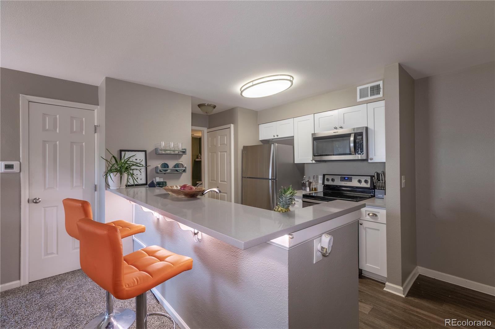 2575 South Syracuse Way, Unit M206 Denver, CO 80231 - Photo 6 of 24 a kitchen with stainless steel appliances kitchen island granite countertop a refrigerator a stove a sink dishwasher and white cabinets with wooden floor