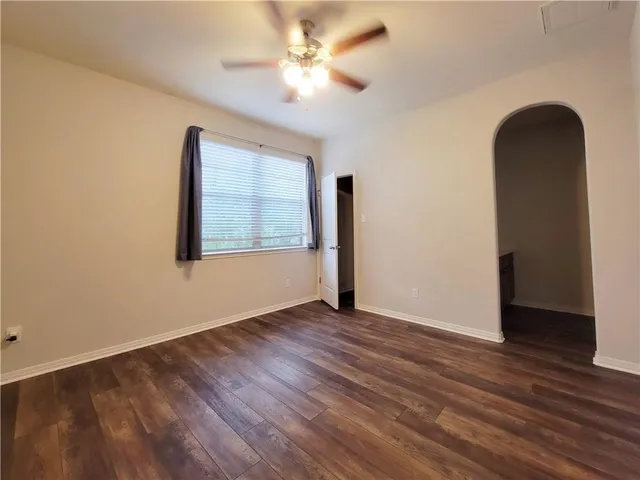 an empty room with wooden floor chandelier fan and windows