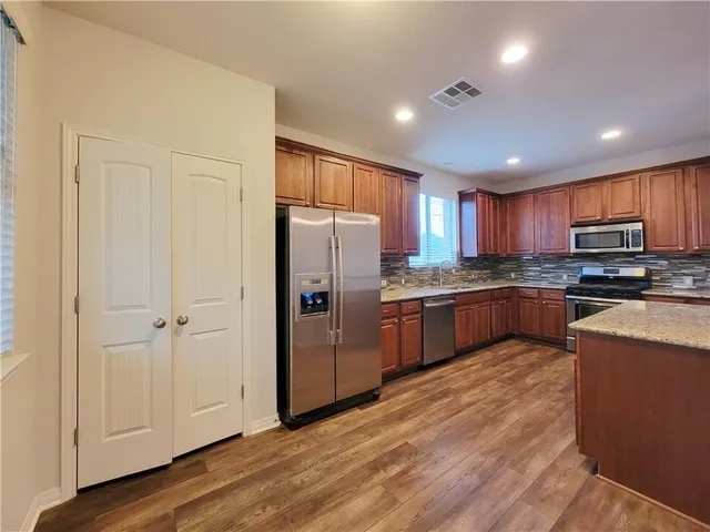 a kitchen with stainless steel appliances granite countertop a refrigerator oven a sink dishwasher and a stove with wooden floor