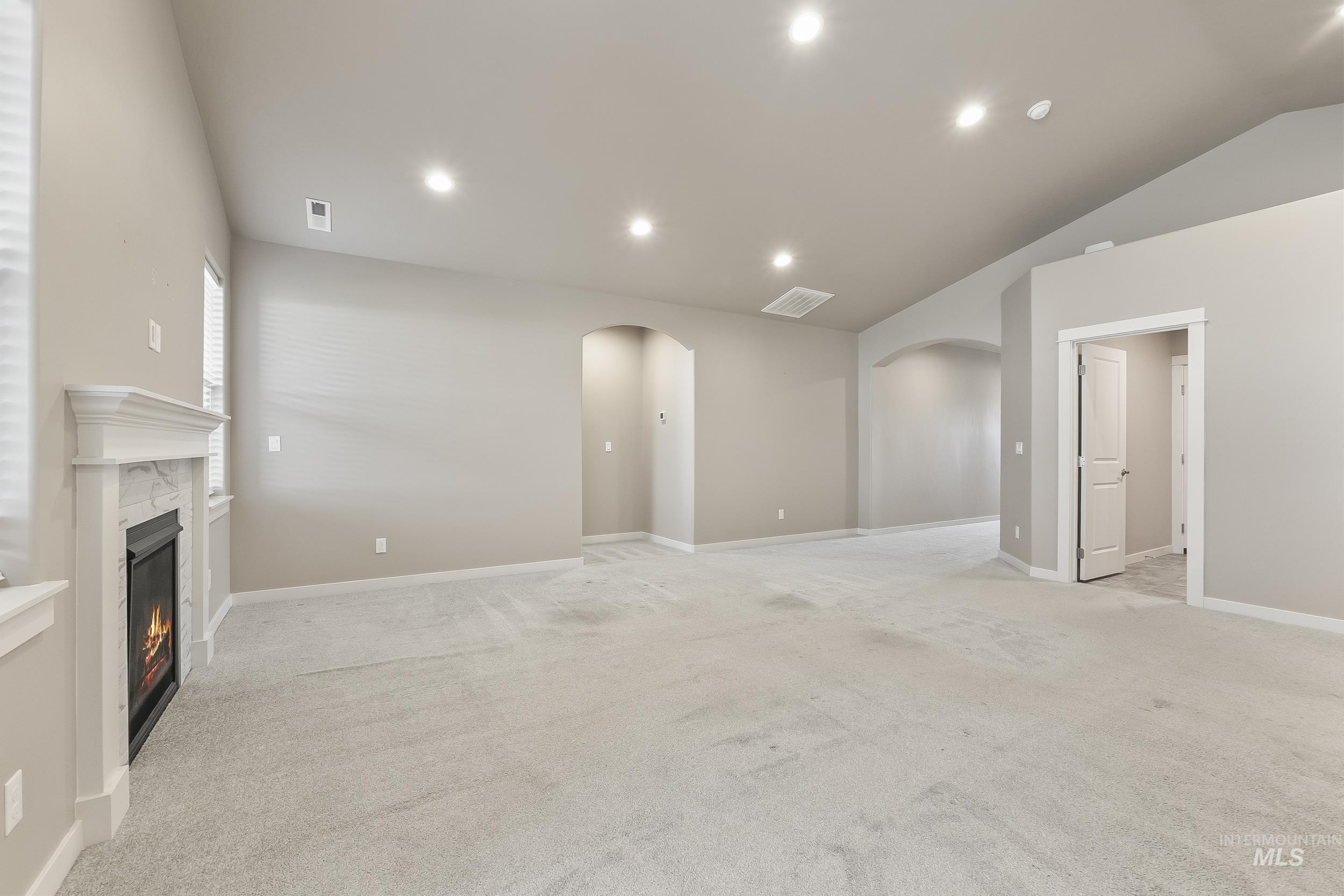 10308 West Trident Ridge Drive Star, ID 83669 - Photo 11 of 42 Unfurnished living room with lofted ceiling, arched walkways, a high end fireplace, light colored carpet, and recessed lighting