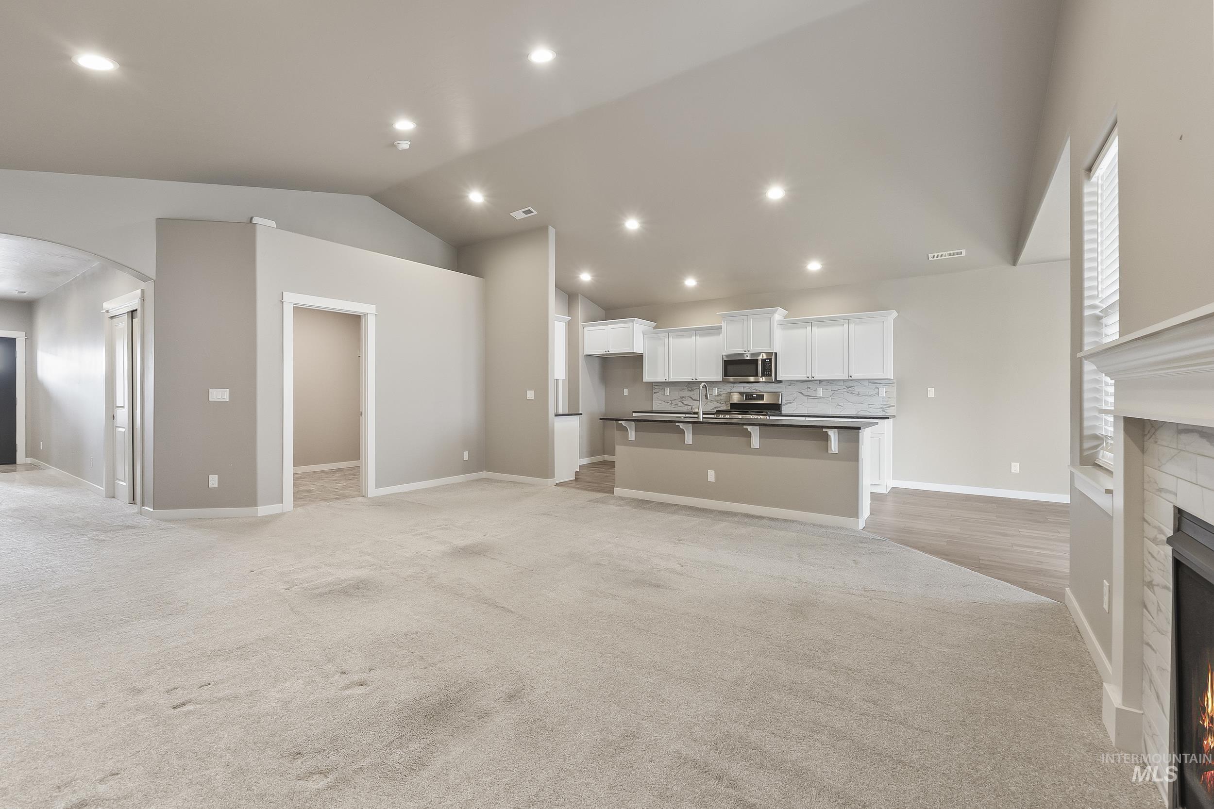 10308 West Trident Ridge Drive Star, ID 83669 - Photo 12 of 42 Unfurnished living room with a warm lit fireplace, arched walkways, light carpet, and recessed lighting