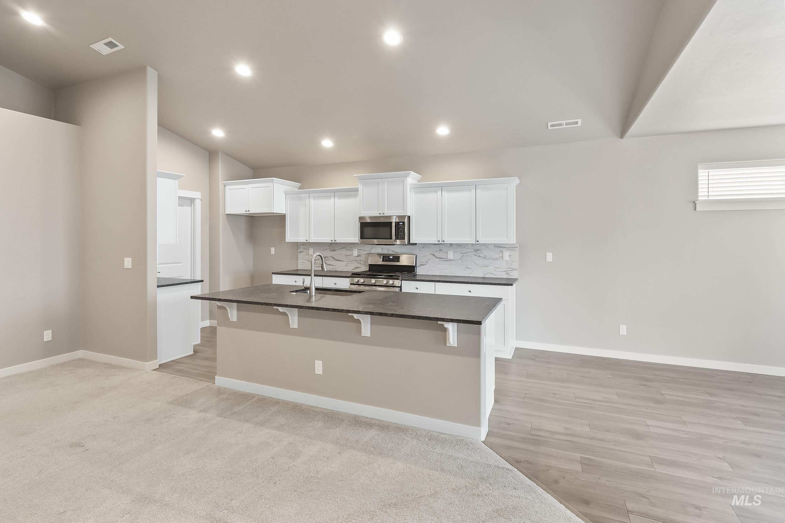 10308 West Trident Ridge Drive Star, ID 83669 - Photo 15 of 42 Kitchen featuring white cabinetry, stainless steel appliances, a kitchen breakfast bar, a kitchen island with sink, and tasteful backsplash