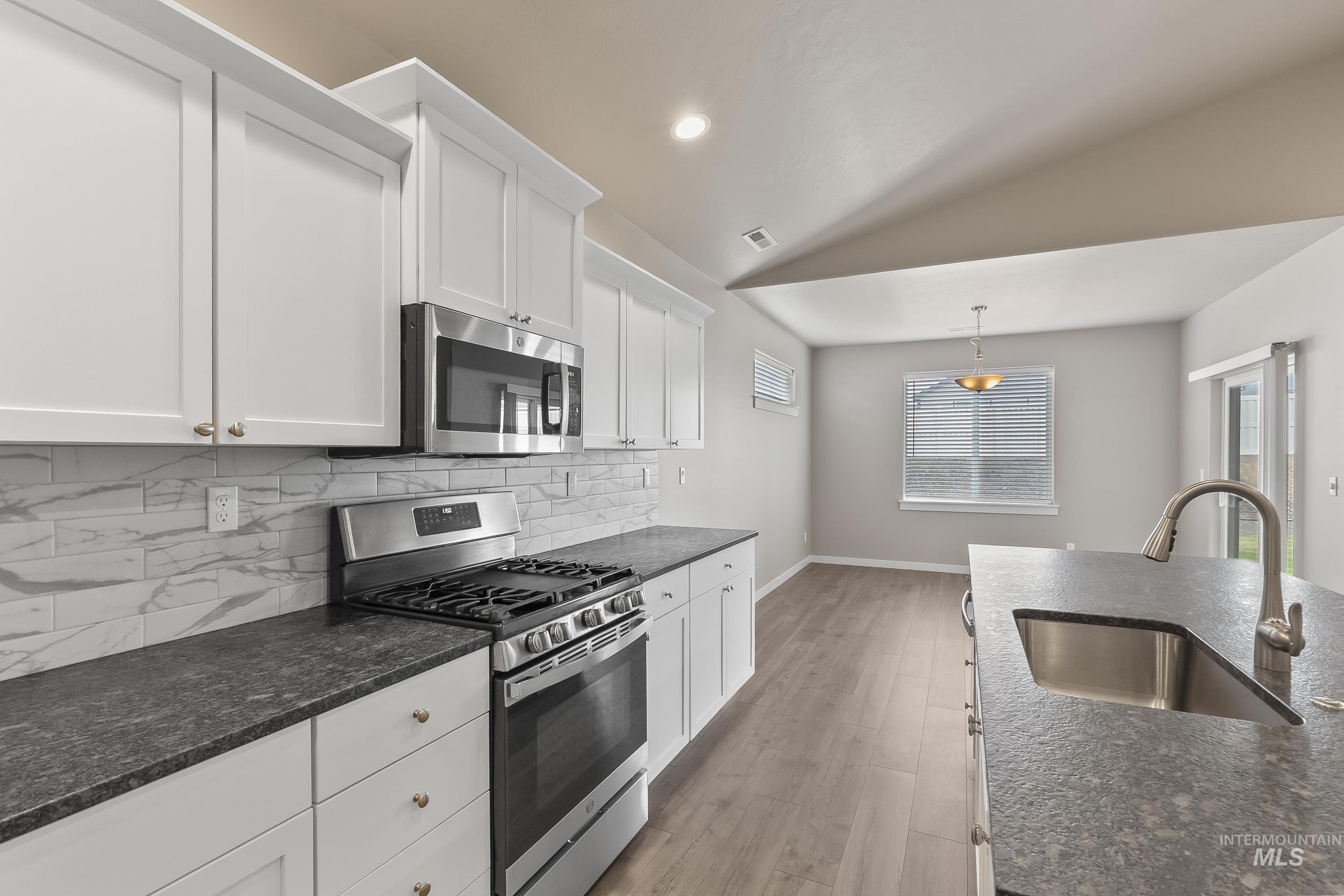 10308 West Trident Ridge Drive Star, ID 83669 - Photo 18 of 42 Kitchen with stainless steel appliances, white cabinetry, decorative backsplash, light wood-style flooring, and vaulted ceiling