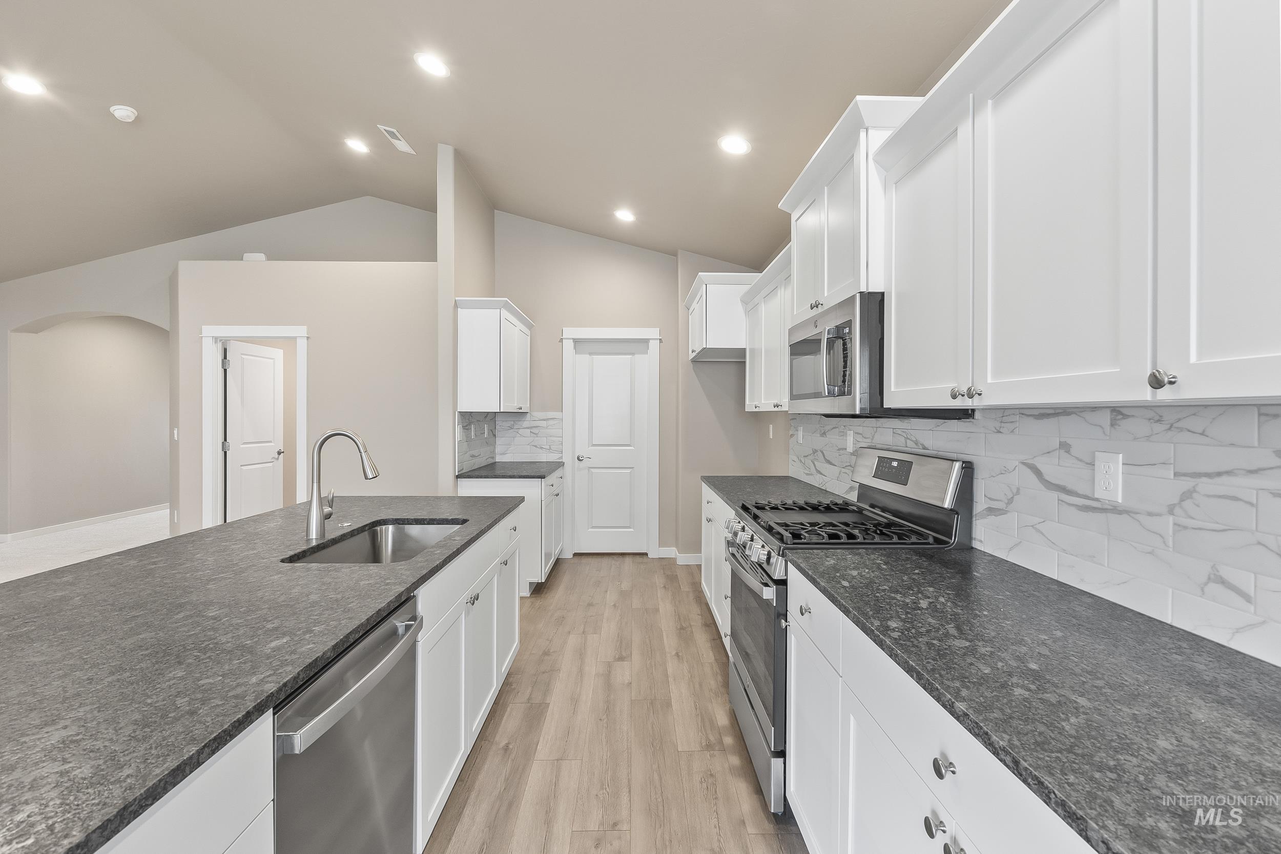 10308 West Trident Ridge Drive Star, ID 83669 - Photo 20 of 42 Kitchen featuring stainless steel appliances, light wood-style floors, backsplash, white cabinetry, and lofted ceiling