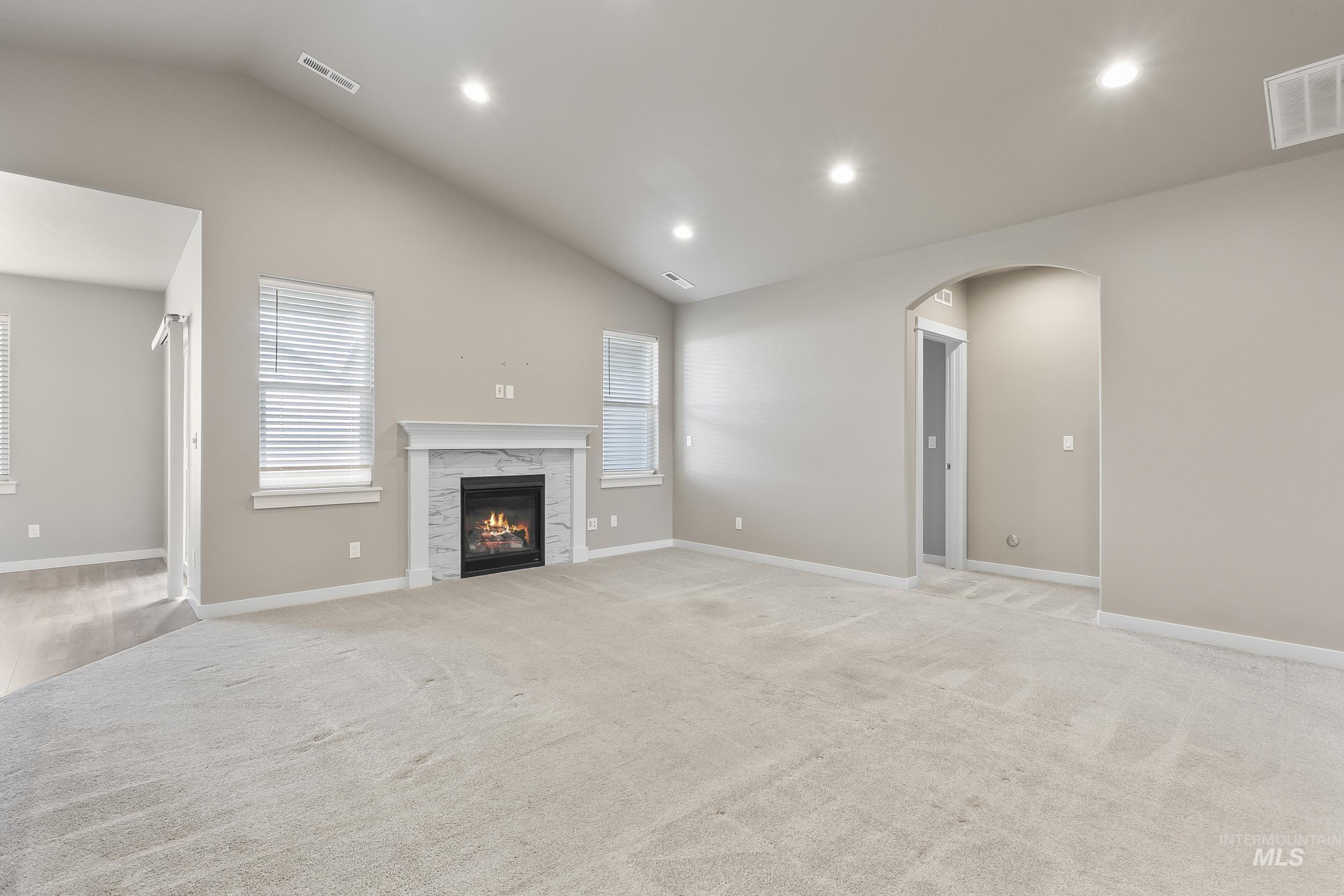 10308 West Trident Ridge Drive Star, ID 83669 - Photo 9 of 42 Unfurnished living room with arched walkways, vaulted ceiling, a high end fireplace, recessed lighting, and light carpet