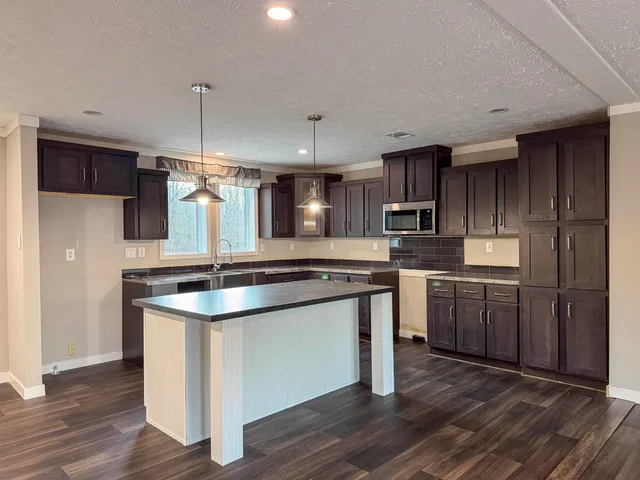 a kitchen with stainless steel appliances granite countertop a sink a stove a refrigerator and island with wooden floor